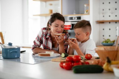 Anne ve oğul kahvaltı hazırlıyorlar. Anne ve oğlu mutfakta sandviç yiyorlar.