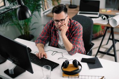 Çalışma masasında gözlüklü ve kareli gömlekli genç bir adam var.