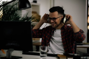 İş masasında kulaklık takan gözlüklü ve kareli gömlekli genç bir adam.