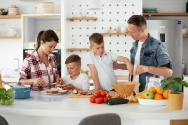 Genç mutlu aile evde sandviç yapıyor. Annem ve babam oğullarımla kahvaltı hazırlıyorlar..