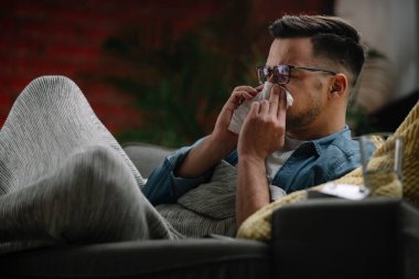 Genç adam evde hasta. Erkek, kanepede yatıyor ve ateşi var..