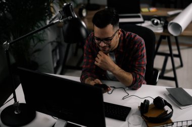 Çalışma masasında gözlüklü ve kareli gömlekli genç bir adam var.