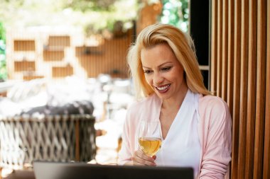 Takım elbiseli, şarap içen ve dizüstü bilgisayarla çalışan güzel bir iş kadını. İş kadını restoranda eğleniyor.