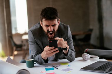 Kızgın iş adamı proje üzerinde çalışıyor. Ofiste akıllı telefon kullanan genç bir işadamı..