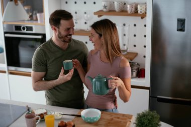 Sevgili çift kahvaltı hazırlarken kahve içiyorlar..