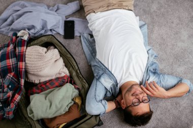 Yolculuğa hazırlanan adam, valizinin yanında yatıyor.