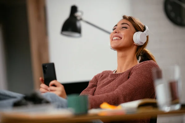 Young woman in office with headphones. Young casual businesswoman enjoying in her favorite song over headphones and singing while working on laptop in the office.