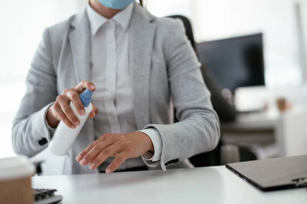 Close up of businesswoman disinfecting hands in the office.