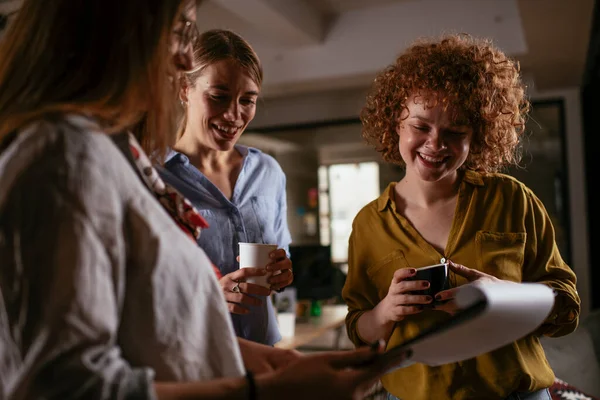 Girls talking and laughing in office. Beautiful women drinking coffee in the office