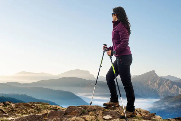 关闭后视图肖像的女远足者站在岩石地形与步行杆 日出时观赏群山的女人 — 图库照片