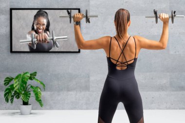 Dambıllarla evde çalışan genç bayanın dikiz aynasından yakından bakın. TV ekranı önünde online ders alan kız.