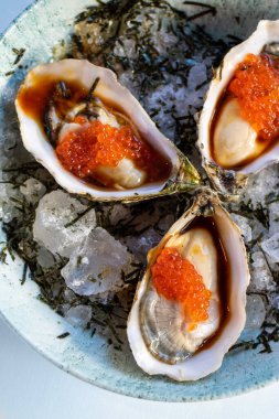 Portakal havyarlı taze istiridye ve ezilmiş buz üzerinde sunulan kırmızı ponzu sosunun dikey üst görüntüsü..