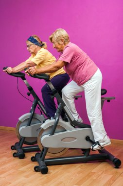 Two golden agers doing spinning in gym. clipart