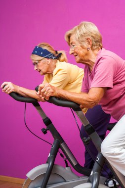 Senior women doing spinning in gym clipart