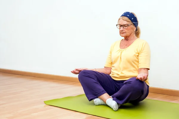 Senior vrouw mediteren in de sportschool. — Stockfoto