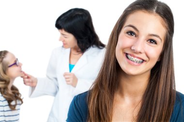 Diş telleri ve doktor hasta arka planda ile genç kız.