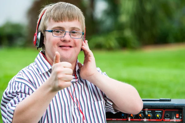 Síndrome de Down chico con auriculares haciendo pulgares hacia arriba . —  Fotos de Stock