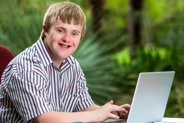 Инвалидный молодой человек печатает на ноутбуке в саду . — стоковое фото