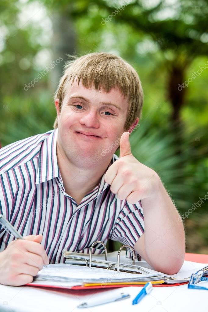 Handicapped boy doing thumbs up at desk outdoors.