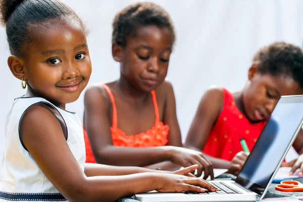 Little African girl doing homework on computer with friends.