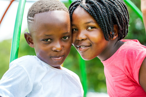 Young African brother and sister joining heads outdoors.