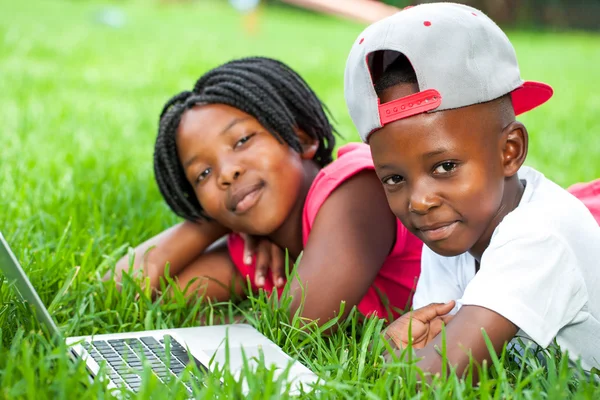 Afrikalı çocuklar dizüstü bilgisayar ile çimenlerin üzerinde döşeme. — Stok fotoğraf