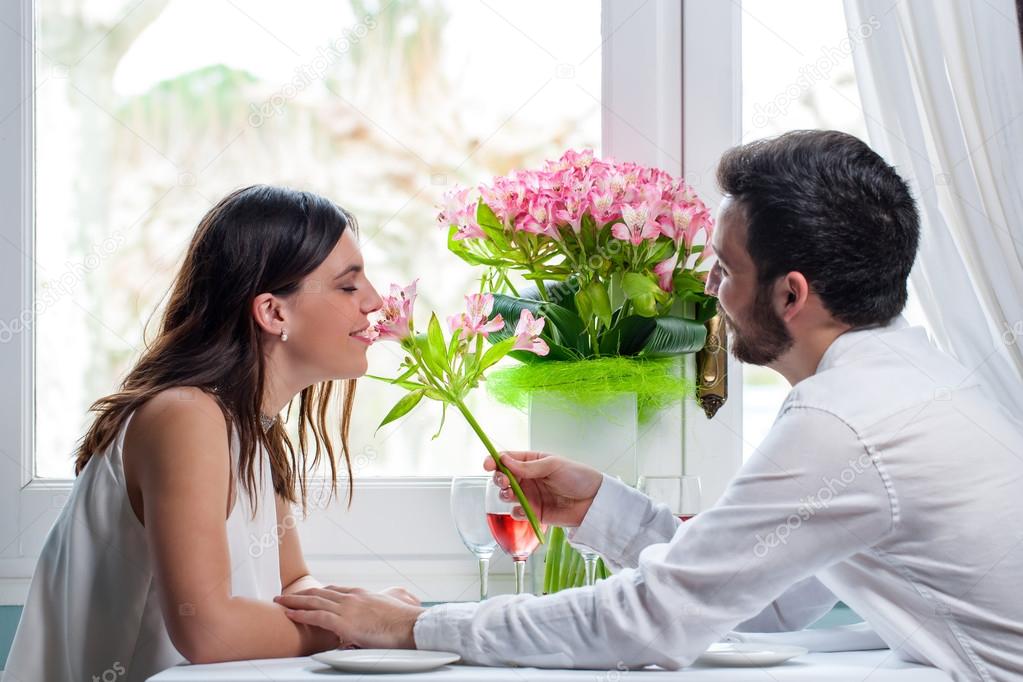 Young man giving flower to girlfriend in restaurant.