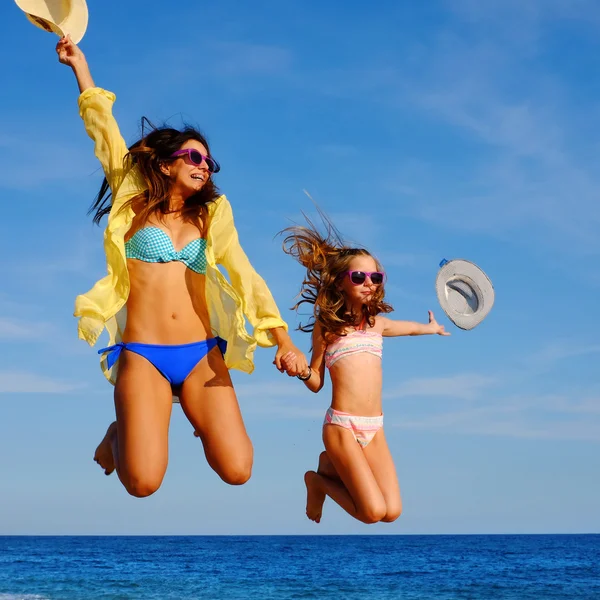Young girls on holiday jumping with hats. — Stock Photo, Image