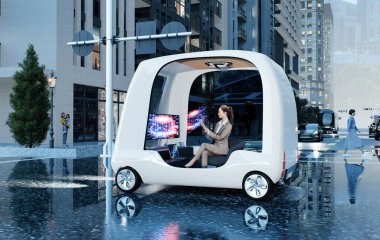 Gelecekçi otonom bir araç yağmurlu bir günde modern bir şehir caddesinden geçiyor. Kompakt, açık tasarım podunun içinde, bir iş kadını veri görselleştirmeleri ve holografik grafikleri gösteren büyük dijital ekranlarla çevrili bir tablet üzerinde çalışıyor.. 