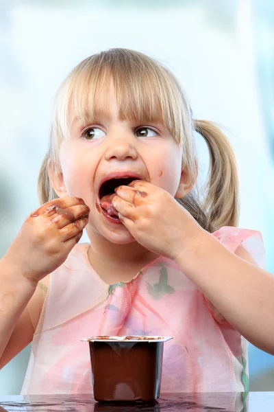 Leuk meisje eten chocolade yoghurt met handen. — Stockfoto