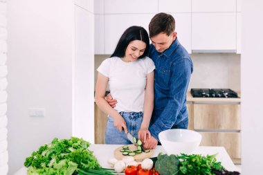 Mutfak tezgahında birlikte sebze doğrayan sevimli genç bir çift. Aşık genç adam ve kadın evde birlikte yemek pişiriyorlar..