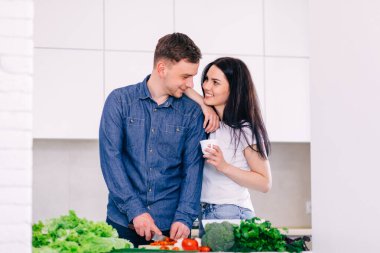 Genç bir adam, kız kahve içerken domatesleri salataya kesiyor..