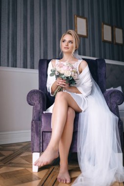 Gelin elinde bir düğün buketi tutuyor. Beyaz bir cübbe ve peçeyle bir sandalyede oturuyor. Uzaklara bakıyorum..