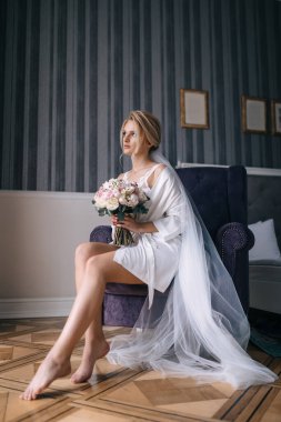 Gelin elinde bir düğün buketi tutuyor. Beyaz bir cübbe ve peçeyle bir sandalyede oturuyor. Uzaklara bakıyorum..