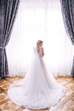 Lüks beyaz elbiseli gelin pencerenin yanında duruyor.