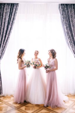 Elinde buketi olan neşeli gelin pembe elbiseli kız arkadaşlarının yanında duruyor.
