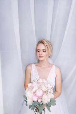 Büyük penceredeki gelin damadı bekliyor. Beyaz elbiseli çekici bir gelin elinde bir buket tutuyor..