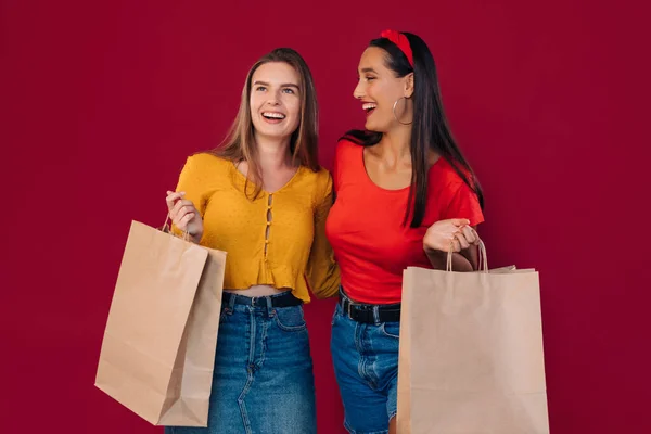 快乐的姑娘们笑着 谈着话 去商店后拿着一个包 在绿色的背景下摆姿势 — 图库照片
