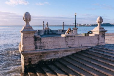Beyaz ceketli gözlüklü bir kız nehir kenarındaki taştan bir bölümde duruyor..