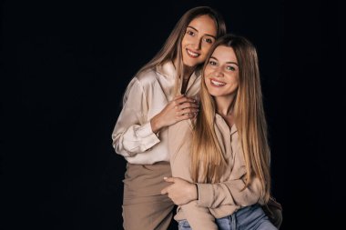 İki neşeli kız kardeş stüdyoda klasik kıyafetler içinde bir sandalyede oturuyorlar. Bir kız diğerine arkadan sarılıyor, elini omzuna koyuyor..