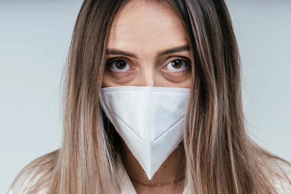 portrait of a beautiful young woman in a cotton white mask on a white background. sadness in the eyes from the outbreak of the disease.