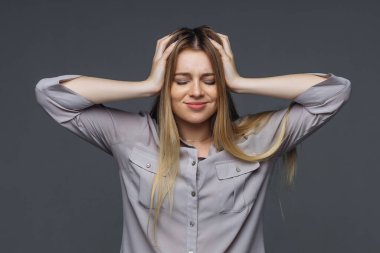 Uzun saçlı, genç ve güzel bir kız izole bir arka planda duruyor ve elleriyle başını tutuyor...