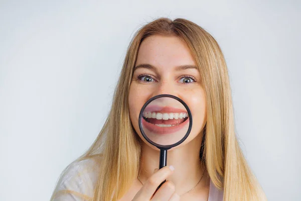 ブロンドは歯の前に虫眼鏡をかけている 明るい笑顔の女の子 歯科治療 — ストック写真