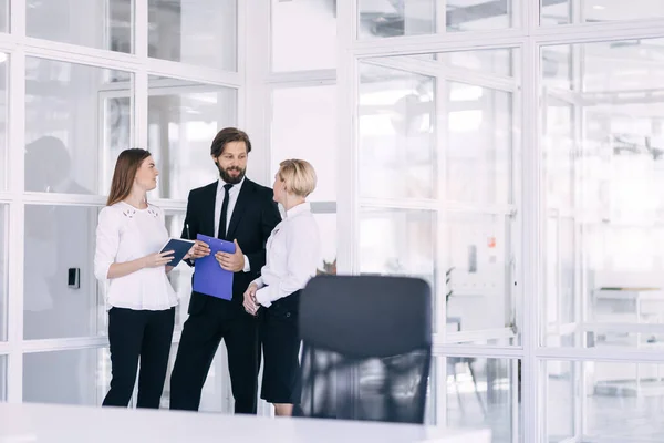 A responsible international business team of three employees analyzes paper project documents in the office.