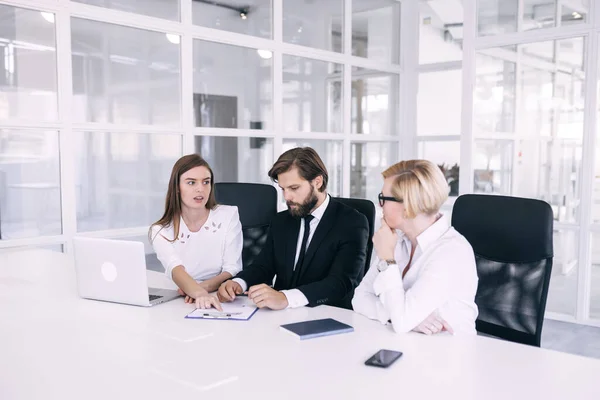 A group of young office workers dressed in business suits doing office work at a large conference table. The girl points to the documents.