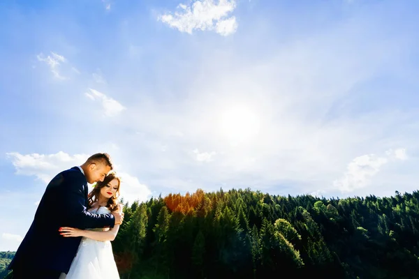 穿着婚纱的新郎和新娘在夏天拥抱的草地上散步 — 图库照片