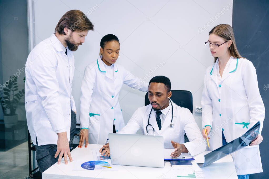The medical team checks the results of x-rays on a laptop in the office. The American doctor seriously discusses and explains the diagnosis to his colleagues.