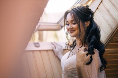 Nazik bir kız. Gelin pencerenin yanında duruyor. Gözleri kapalı ve bukleli gülüyor.