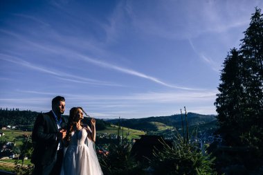 göz kamaştırıcı yeni evliler ormanda yürüyorlar mavi gökyüzünün arka planına ve güzel doğaya bakıyorlar..