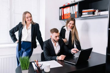 Modern ofiste çalışan genç iş adamları, iş arkadaşları dizüstü bilgisayarla projeyi tartışıyor, küçük iş adamları gülümsüyor ve birlikte bilgisayara bakıyorlar.